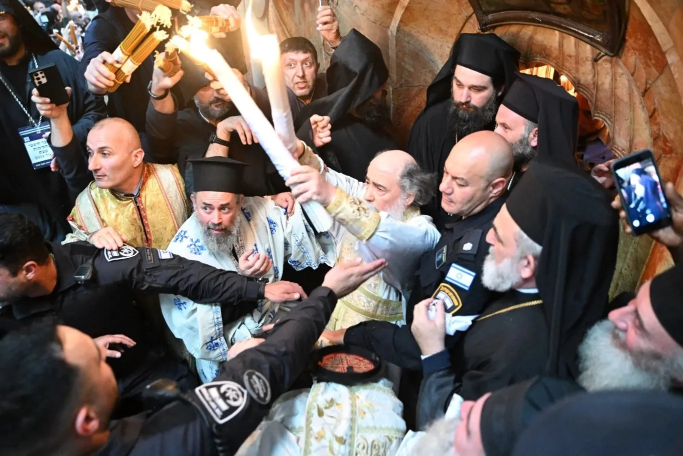 De Grieks-orthodoxe patriarch Theophilos III verlaat de Aedicule van het Heilig Graf op 4 mei 2024 in Jeruzalem. Hij laat de gelovigen de twee kaarsen zien die net zijn aangestoken aan het vuur van de olielamp waarvan wordt geloofd dat dit op miraculeuze wijze zou zijn ontbrand in het graf van Jezus. Met dank aan: Studio Sami Jeruzalem